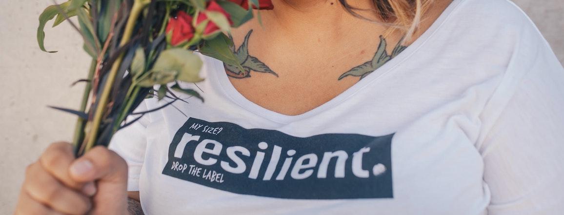 Person holding flowers and wearing a shirt that reads "My size? Resilient. Drop the label."